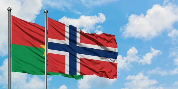 Burkina Faso y la bandera de Noruega ondeando en el viento contra el cielo azul nublado blanco juntos. Concepto diplomático, relaciones internacionales . — Foto de Stock