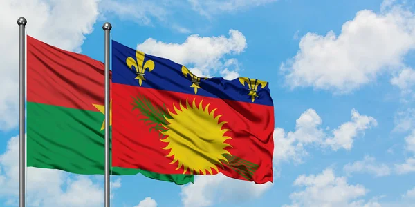 Bandera de Burkina Faso y Guadalupe ondeando en el viento contra el cielo azul nublado blanco juntos. Concepto diplomático, relaciones internacionales . — Foto de Stock