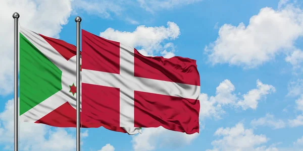 Burundi a Dánská vlajka mávali ve větru proti bíle zatažené modré obloze. Diplomacie, mezinárodní vztahy. — Stock fotografie