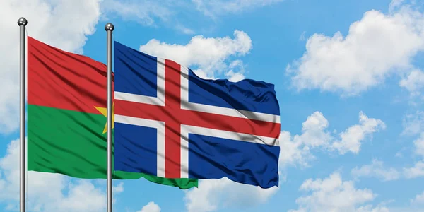 Burkina Faso y la bandera de Islandia ondeando en el viento contra el cielo azul nublado blanco juntos. Concepto diplomático, relaciones internacionales . — Foto de Stock