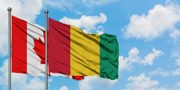 Bandera de Canadá y Guinea ondeando en el viento contra el cielo azul nublado blanco juntos. Concepto diplomático, relaciones internacionales . — Foto de Stock