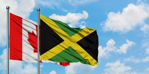 Bandera de Canadá y Jamaica ondeando en el viento contra el cielo azul nublado blanco juntos. Concepto diplomático, relaciones internacionales . — Foto de Stock