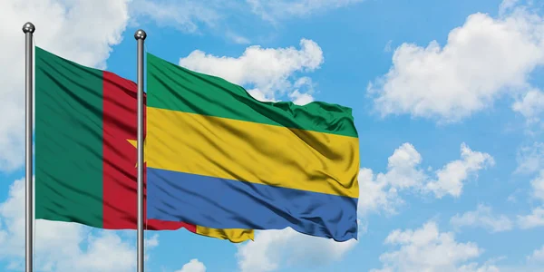Bandera de Camerún y Gabón ondeando en el viento contra el cielo azul nublado blanco juntos. Concepto diplomático, relaciones internacionales . — Foto de Stock