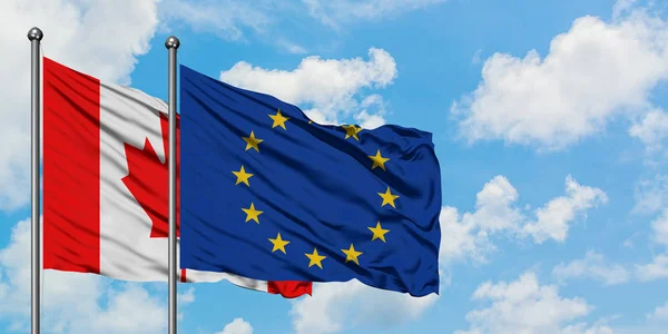 Bandera de Canadá y la Unión Europea ondeando en el viento contra el cielo azul nublado blanco juntos. Concepto diplomático, relaciones internacionales . — Foto de Stock