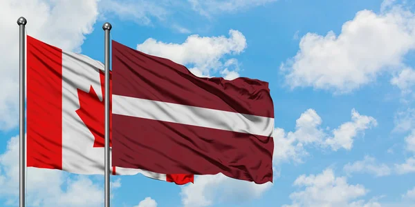 Kanada a Lotyšsko vlají ve větru proti bíle zatažené modré obloze. Diplomacie, mezinárodní vztahy. — Stock fotografie