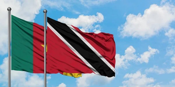 Kamerun ve Trinidad ve Tobago bayrağı birlikte beyaz bulutlu mavi gökyüzüne karşı rüzgarda sallayarak. Diplomasi kavramı, uluslararası ilişkiler. — Stok fotoğraf