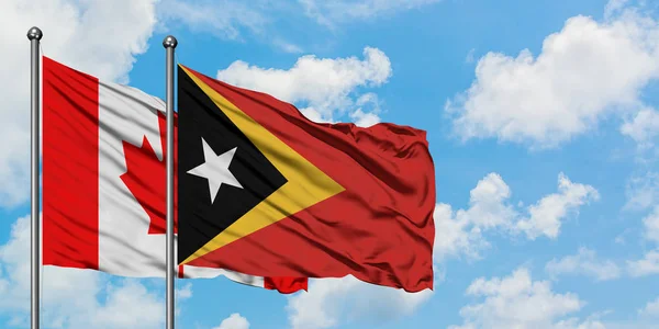 Bandera de Canadá y Timor Oriental ondeando en el viento contra el cielo azul nublado blanco juntos. Concepto diplomático, relaciones internacionales . — Foto de Stock