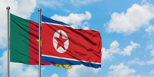 Bandera de Camerún y Corea del Norte ondeando en el viento contra el cielo azul nublado blanco juntos. Concepto diplomático, relaciones internacionales . — Foto de Stock