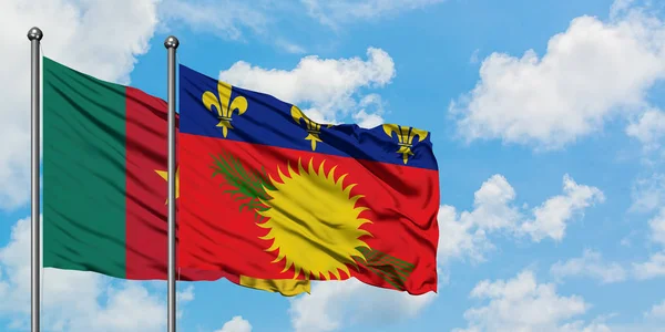 Bandera de Camerún y Guadalupe ondeando en el viento contra el cielo azul nublado blanco juntos. Concepto diplomático, relaciones internacionales . — Foto de Stock