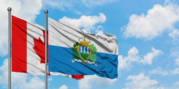 Bandera de Canadá y San Marino ondeando en el viento contra el cielo azul nublado blanco juntos. Concepto diplomático, relaciones internacionales . — Foto de Stock