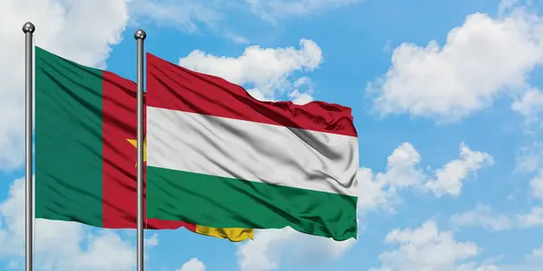 Bandera de Camerún y Hungría ondeando en el viento contra el cielo azul nublado blanco juntos. Concepto diplomático, relaciones internacionales . — Foto de Stock