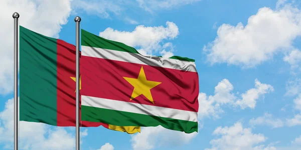 Bandera de Camerún y Surinam ondeando en el viento contra el cielo azul nublado blanco juntos. Concepto diplomático, relaciones internacionales . — Foto de Stock