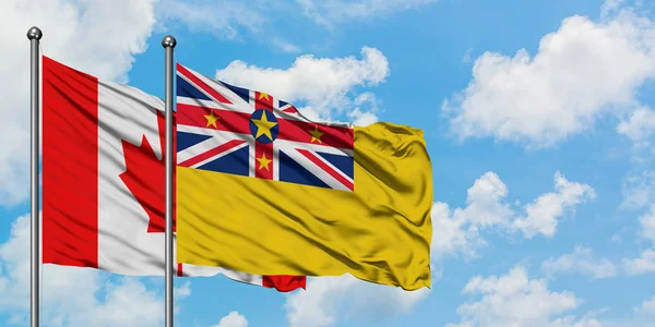 Bandera de Canadá y Niue ondeando en el viento contra el cielo azul nublado blanco juntos. Concepto diplomático, relaciones internacionales . — Foto de Stock