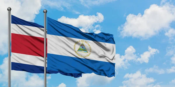 Bandera de Costa Rica y Nicaragua ondeando en el viento contra el cielo azul nublado blanco juntos. Concepto diplomático, relaciones internacionales . — Foto de Stock