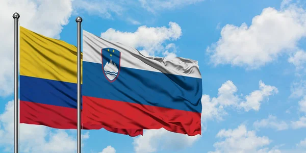 Bandera de Colombia y Eslovenia ondeando en el viento contra el cielo azul nublado blanco juntos. Concepto diplomático, relaciones internacionales . — Foto de Stock