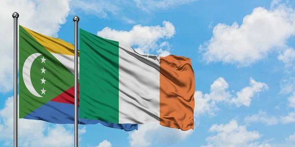 Bandera de las Comoras e Irlanda ondeando en el viento contra el cielo azul nublado blanco juntos. Concepto diplomático, relaciones internacionales . — Foto de Stock