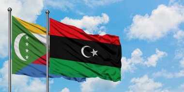 Komorlar ve Libya bayrağı birlikte beyaz bulutlu mavi gökyüzüne karşı rüzgarda sallayarak. Diplomasi kavramı, uluslararası ilişkiler.