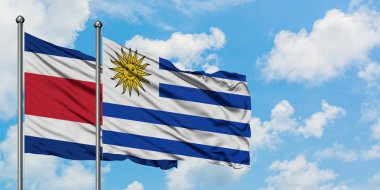 Kosta Rika ve Uruguay bayrağı birlikte beyaz bulutlu mavi gökyüzüne karşı rüzgarda sallayarak. Diplomasi kavramı, uluslararası ilişkiler.