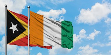 Doğu Timor ve Fildişi Sahili bayrağı birlikte beyaz bulutlu mavi gökyüzüne karşı rüzgarda sallayarak. Diplomasi kavramı, uluslararası ilişkiler.