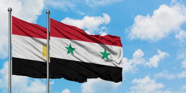 Mısır ve Suriye bayrağı birlikte beyaz bulutlu mavi gökyüzüne karşı rüzgarsal sallayarak. Diplomasi kavramı, uluslararası ilişkiler.