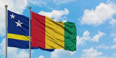 Curacao ve Gine bayrağı birlikte beyaz bulutlu mavi gökyüzüne karşı rüzgarda sallayarak. Diplomasi kavramı, uluslararası ilişkiler.