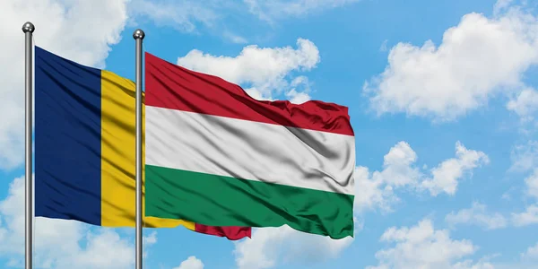 Bandera de Chad y Hungría ondeando en el viento contra el cielo azul nublado blanco juntos. Concepto diplomático, relaciones internacionales . — Foto de Stock
