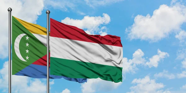 Bandera de las Comoras y Hungría ondeando en el viento contra el cielo azul nublado blanco juntos. Concepto diplomático, relaciones internacionales . —  Fotos de Stock