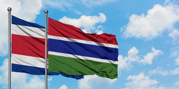 Costa Rica- und Gambia-Flagge wehen gemeinsam im Wind vor dem wolkenverhangenen blauen Himmel. Diplomatie-Konzept, internationale Beziehungen. — Stockfoto