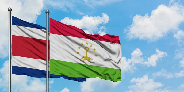 Bandera de Costa Rica y Tayikistán ondeando en el viento contra el cielo azul nublado blanco juntos. Concepto diplomático, relaciones internacionales . — Foto de Stock