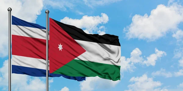 Bandera de Costa Rica y Jordania ondeando en el viento contra el cielo azul nublado blanco juntos. Concepto diplomático, relaciones internacionales . — Foto de Stock