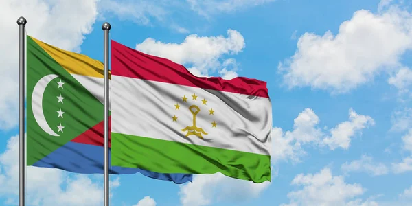 Bandera de Comoras y Tayikistán ondeando en el viento contra el cielo azul nublado blanco juntos. Concepto diplomático, relaciones internacionales . — Foto de Stock