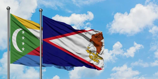 Comoras y la bandera de Samoa Americana ondeando en el viento contra el cielo azul nublado blanco juntos. Concepto diplomático, relaciones internacionales . — Foto de Stock