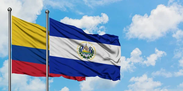 A Colômbia e a bandeira de El Salvador acenando ao vento contra o céu azul nublado branco juntas. Conceito de diplomacia, relações internacionais . — Fotografia de Stock