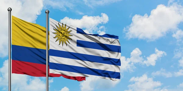 Bandera de Colombia y Uruguay ondeando en el viento contra el cielo azul nublado blanco juntos. Concepto diplomático, relaciones internacionales . —  Fotos de Stock