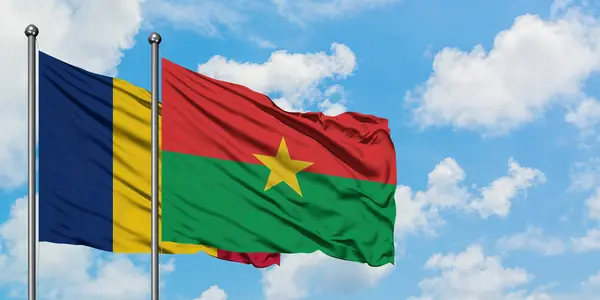 Bandera Chad y Burkina Faso ondeando en el viento contra el cielo azul nublado blanco juntos. Concepto diplomático, relaciones internacionales . — Foto de Stock