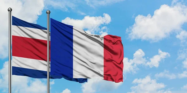 Costa Rica e Francia bandiera sventolando nel vento contro bianco cielo blu nuvoloso insieme. Concetto di diplomazia, relazioni internazionali . — Foto Stock