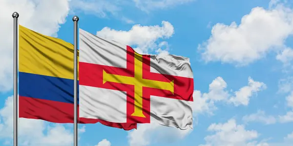 Bandera de Colombia y Guernsey ondeando en el viento contra el cielo azul nublado blanco juntos. Concepto diplomático, relaciones internacionales . — Foto de Stock