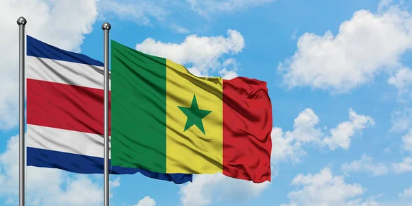 Bandera de Costa Rica y Senegal ondeando en el viento contra el cielo azul nublado blanco juntos. Concepto diplomático, relaciones internacionales . — Foto de Stock