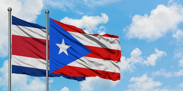Costa Ricas und Puerto Ricos Flagge weht gemeinsam im Wind gegen den wolkenverhangenen blauen Himmel. Diplomatie-Konzept, internationale Beziehungen. — Stockfoto