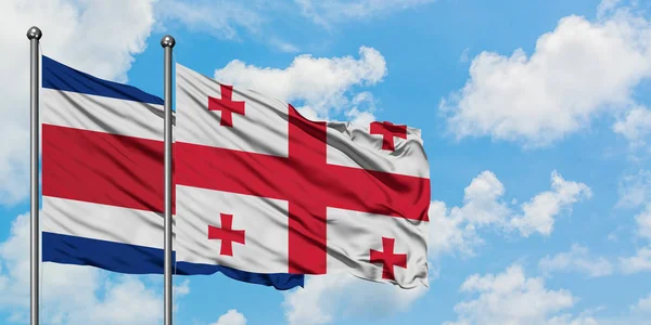 Bandera de Costa Rica y Georgia ondeando en el viento contra el cielo azul nublado blanco juntos. Concepto diplomático, relaciones internacionales . — Foto de Stock