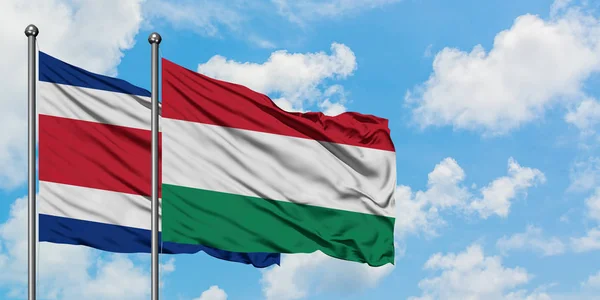 Bandera de Costa Rica y Hungría ondeando en el viento contra el cielo azul nublado blanco juntos. Concepto diplomático, relaciones internacionales . — Foto de Stock