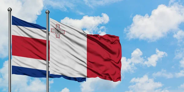 Costa Rica e Malta sventolano bandiera nel vento contro bianco cielo blu nuvoloso insieme. Concetto di diplomazia, relazioni internazionali . — Foto Stock