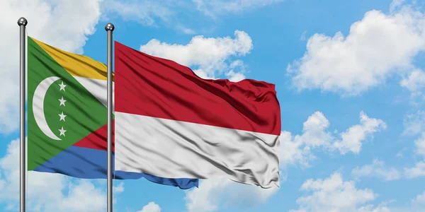 Bandera de las Comoras y Mónaco ondeando en el viento contra el cielo azul nublado blanco juntos. Concepto diplomático, relaciones internacionales . — Foto de Stock