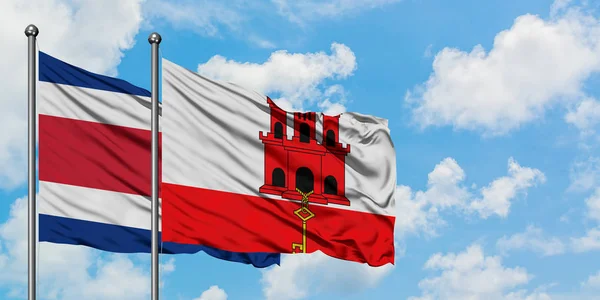Коста-Ріка і прапор Гібралтару розмахуючи в вітру проти білого хмарного синього неба разом. Концепція дипломатії, міжнародні відносини. — стокове фото
