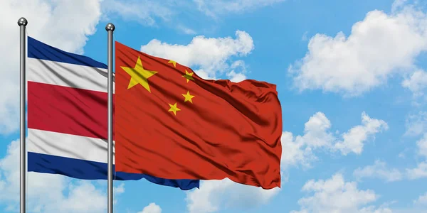 Bandera de Costa Rica y China ondeando en el viento contra el cielo azul nublado blanco juntos. Concepto diplomático, relaciones internacionales . — Foto de Stock