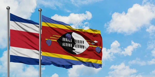 Bandera de Costa Rica y Swazilandia ondeando en el viento contra el cielo azul nublado blanco juntos. Concepto diplomático, relaciones internacionales . — Foto de Stock