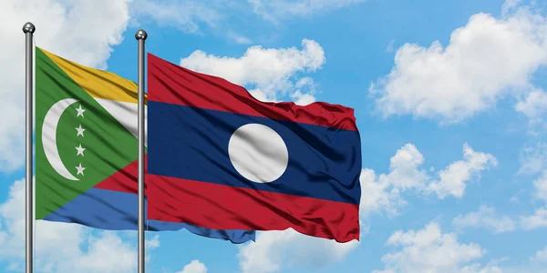 Bandera de las Comoras y Laos ondeando en el viento contra el cielo azul nublado blanco juntos. Concepto diplomático, relaciones internacionales . — Foto de Stock