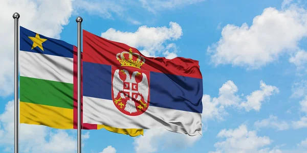 Bandera de la República Centroafricana y Serbia ondeando en el viento contra el cielo azul nublado blanco juntos. Concepto diplomático, relaciones internacionales . — Foto de Stock