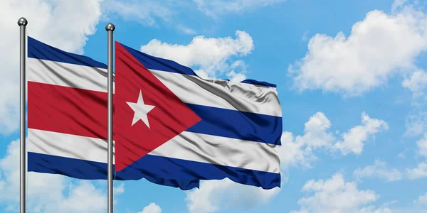 Bandera de Costa Rica y Cuba ondeando en el viento contra el cielo azul nublado blanco juntos. Concepto diplomático, relaciones internacionales . — Foto de Stock