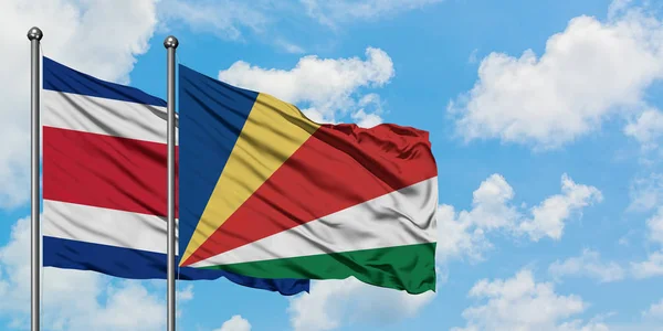 Bandera de Costa Rica y Seychelles ondeando en el viento contra el cielo azul nublado blanco juntos. Concepto diplomático, relaciones internacionales . — Foto de Stock